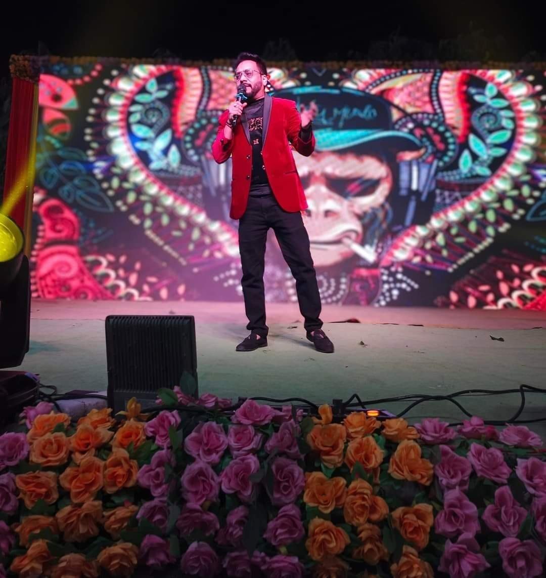 Male singer in a red blazer performing in front of a large LED video wall on an outdoor stage